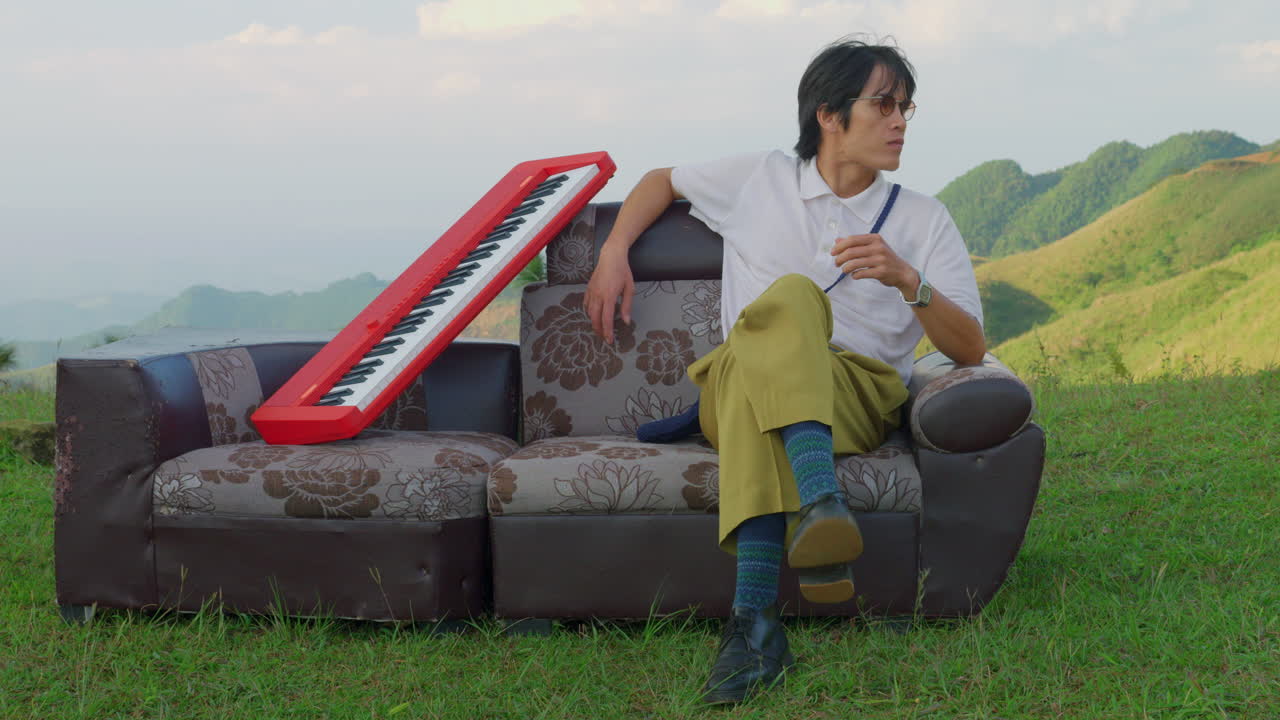 young artist looking for inspiration for a new song album melody while sitting outdoor in a couch with a piano keyboard