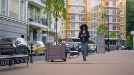 mujer alegre caminando enviando mensajes de texto a amigos en línea. distrito residencial moderno.