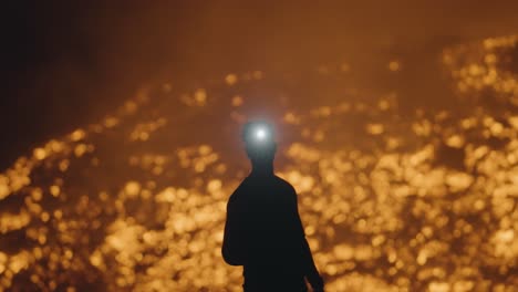 a man’s silhouette, illuminated by a headlamp, hikes at night among the rivers of lava from pacaya volcano in guatemala - handheld shot