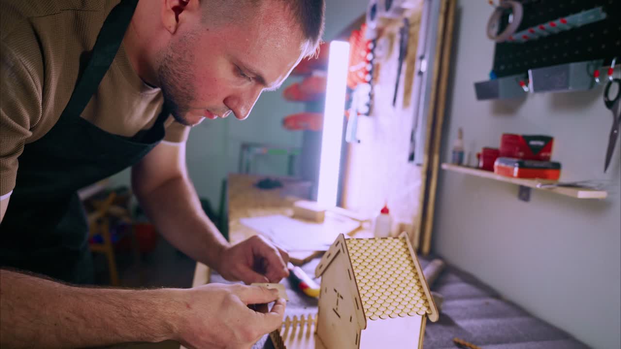 Man Assembling a Wooden Model House in a Workshop