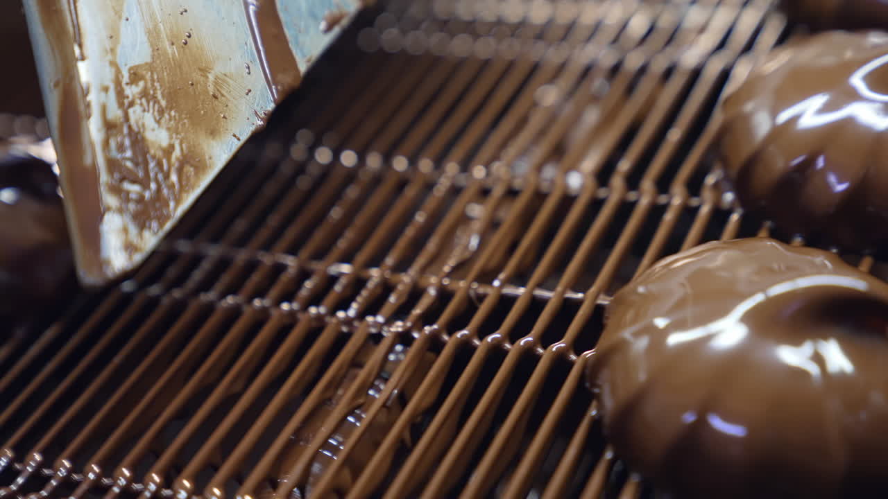 Marshmallows coated with liquid chocolate move under the flow of air. Chocolate desserts on the conveyor grid. Close up.