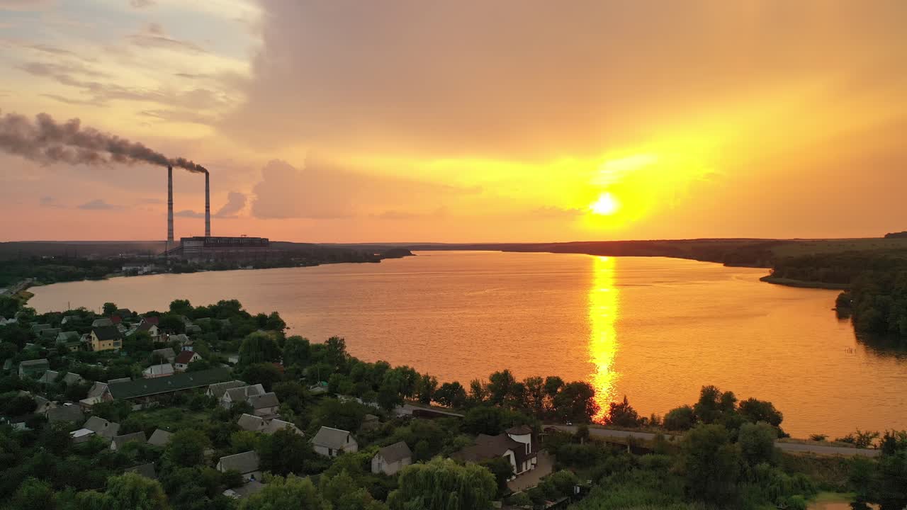 Aerial view of rural place at orange sunset. Golden path of evening sun reflects in the water. Panoramic view of countryside. Camera moves left.