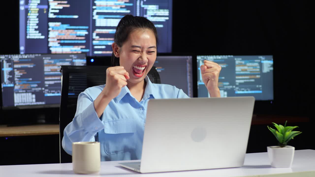 아시아 여성 프로그래머는 여러 모니터를 사용하여 노트북으로 코드를 작성하는 성공을 축하합니다. 사무실의 터미널 윈도우 데스크에서 데이터베이스를 표시합니다.