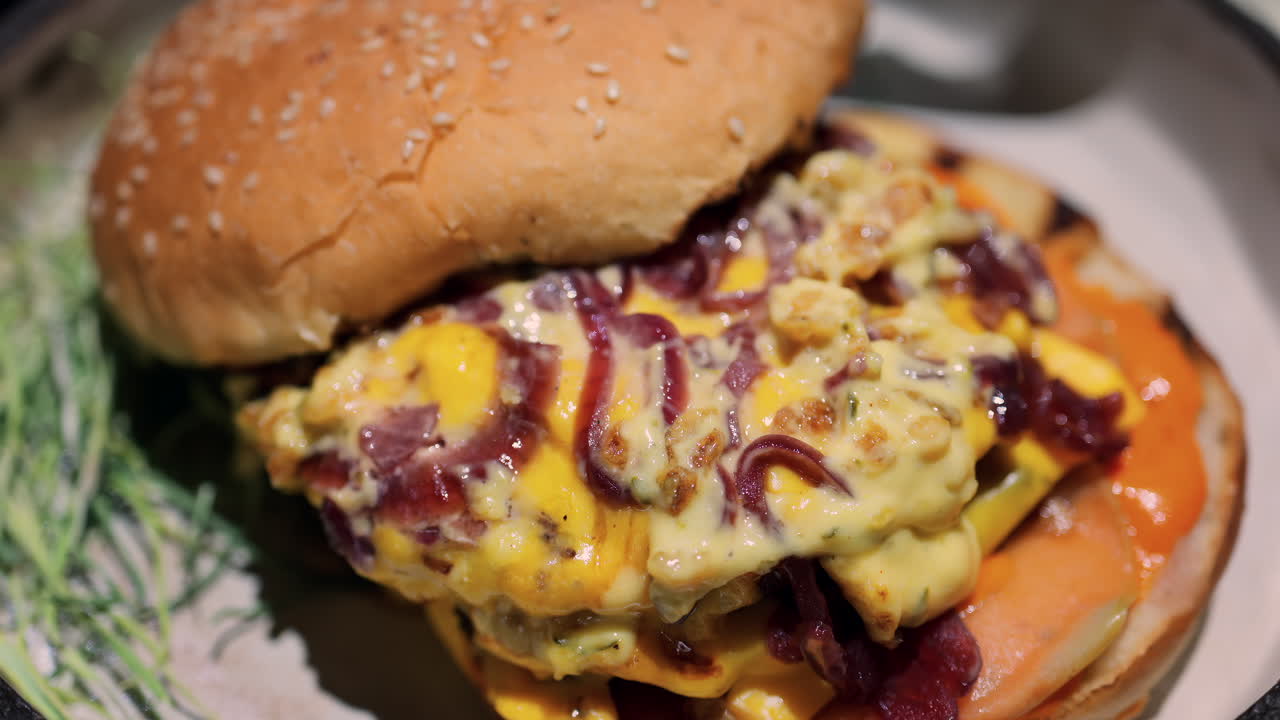 Close up of a loaded burger with melted cheese, caramelised onions, and a creamy sauce on a toasted bun