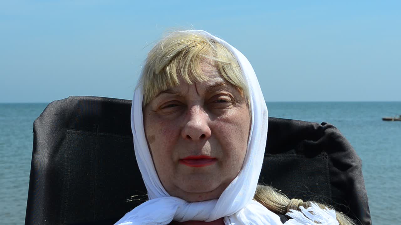 La donna in età pensionabile su una sedia al mare. Riposo della donna al mare.