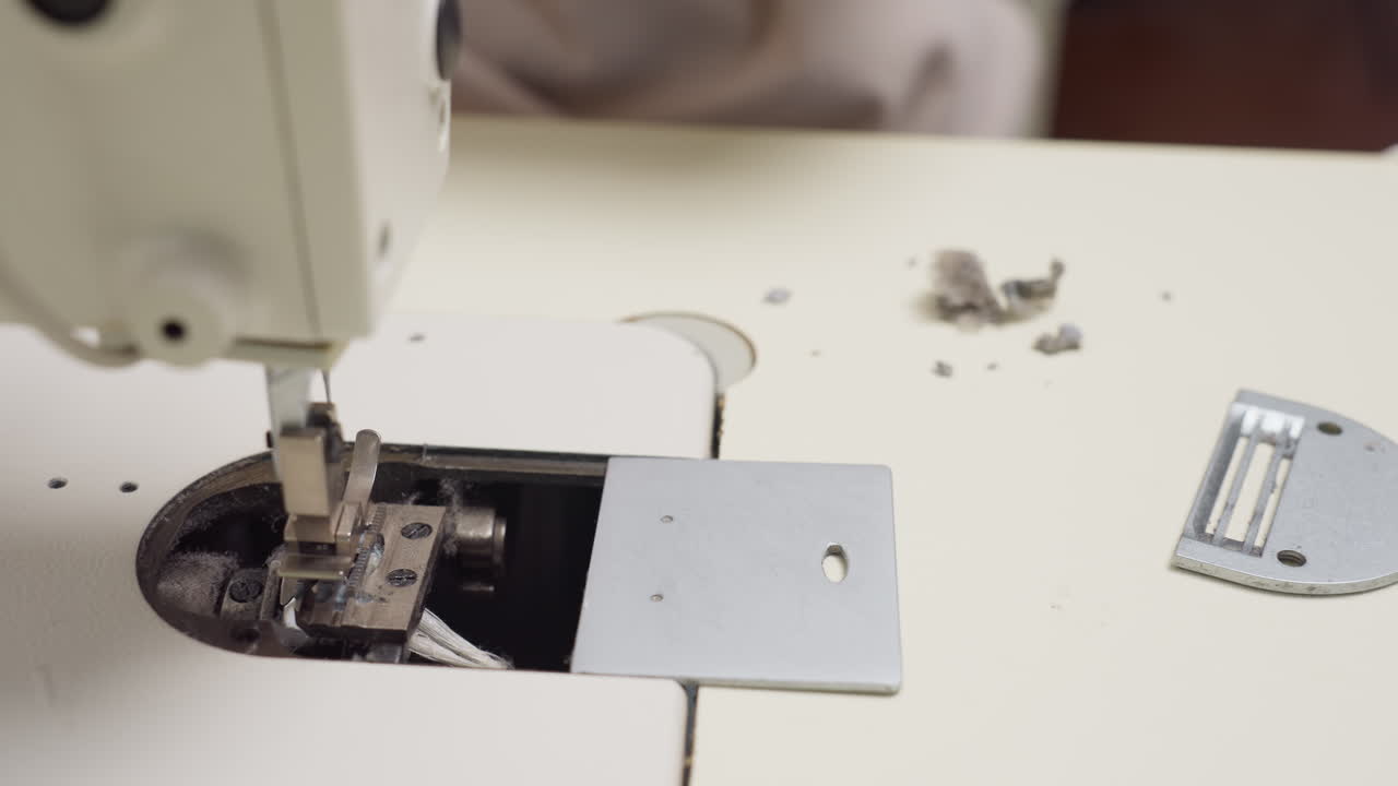 Seamstress cuts out excess thread stuck inside bobbin compartment of sewing machine focusing on detailed cleanup process to ensure smooth sewing operation and proper machine maintenance
