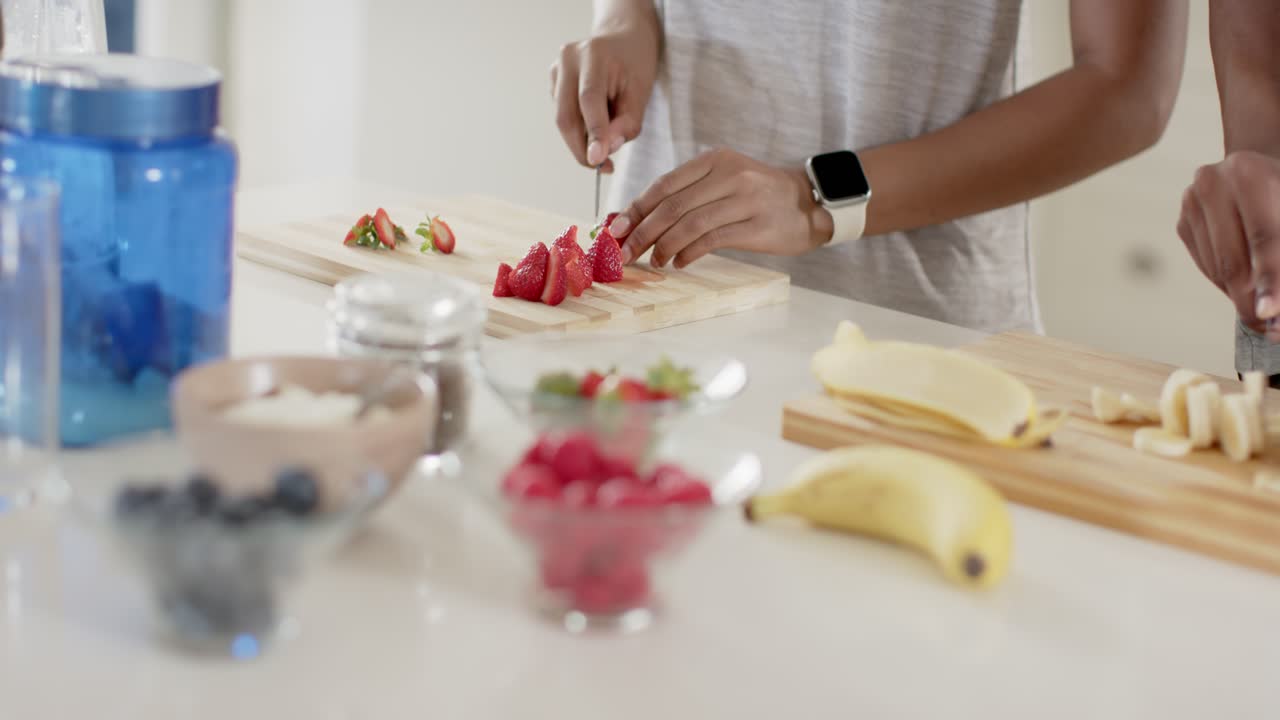 Coppia che pulisce, affetta e dispone le fragole sul bancone della cucina mentre il partner affetta una banana per la ciotola.