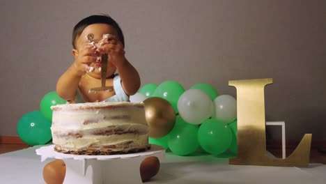 lindo bebé latino celebrando su primer año quitando el número uno de su pastel con globos verdes en el fondo