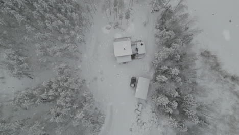 aerial zooming out of snow falling on cabin in a winter wonderland