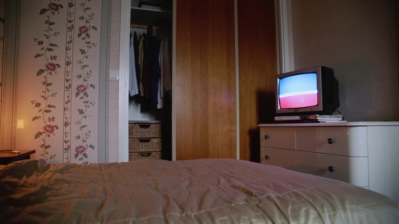 Letto con piumino beige in primo piano in una camera da letto, con il segnale di una TV CRT che cambia bande di colore.