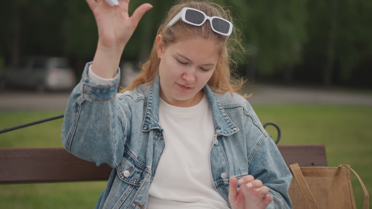 Donna che strappa carta. Donna con giacca di jeans all'aperto. Donna pensierosa che strappa pagine di diario all'esterno. Donna contemplativa in giacca di jeans che strappa pagine di diario in un paesaggio di parco sotto una luce solare soffusa.