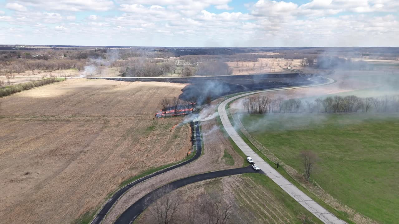 Smoke rolls across fields and a road as men start controlled burns in preparation of a fast-moving wildfire.