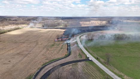 smoke rolls across fields and a road as men start controlled burns in preparation of a fast-moving wildfire.