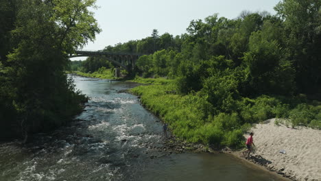 people walking in the river flowing through the green forest near the bridge