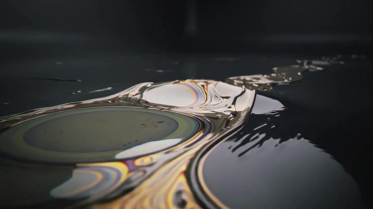 Tracking camera showing thin iridescent film stretching and flowing toward right on dark surface