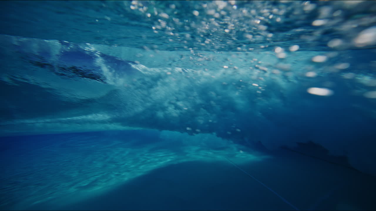 Slow motion underwater view of wave forming in wavepool, with dynamic reflections and mesmerizing water patterns as sunlight sparkles in clear blue barrel