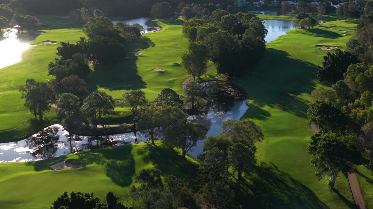 Aerial footage captures a lush golf course with vibrant greens and reflective water features under warm, golden sunlight