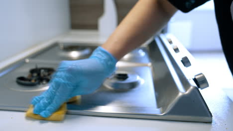 cleaning a kitchen stove with care. a gloved hand wipes down a stainless steel kitchen stove with a sponge, ensuring cleanliness after cooking