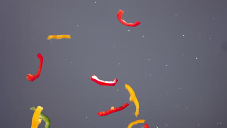 cámara lenta pimienta en rodajas frescas volando junto con gotas de agua en un fondo brillante. disparado con cámara de alta velocidad, 420 fps