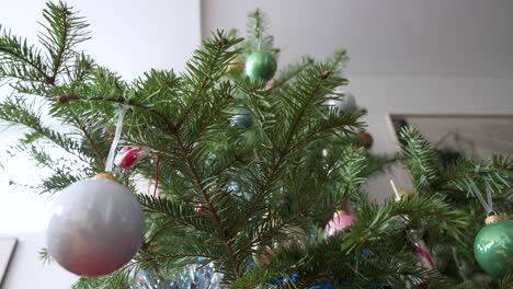 White-and-green-Christmas-balls-stands-out-in-the-foreground,-surrounded-by-ornaments-hanging-from-a-beautifully-decorated-pine-tree,-adding-to-the-winter-festivities