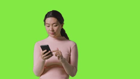 studio shot of woman checking mobile phone and getting good news message against green screen 1