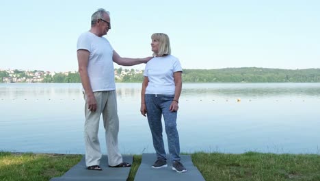 elderly european couple in sportswear talking after morning exercise while standing by the lake happy elderly european couple in sportswear talking after morning exercise while standing by the lake sport in retirement age