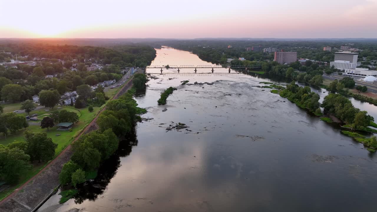 Golden sunset at horizon between Trenton, New Jersey and Morrisville,PA . Reflection on Delaware River with green island and bridge. Aerial backwards wide shot. peaceful serene atmosphere in summer