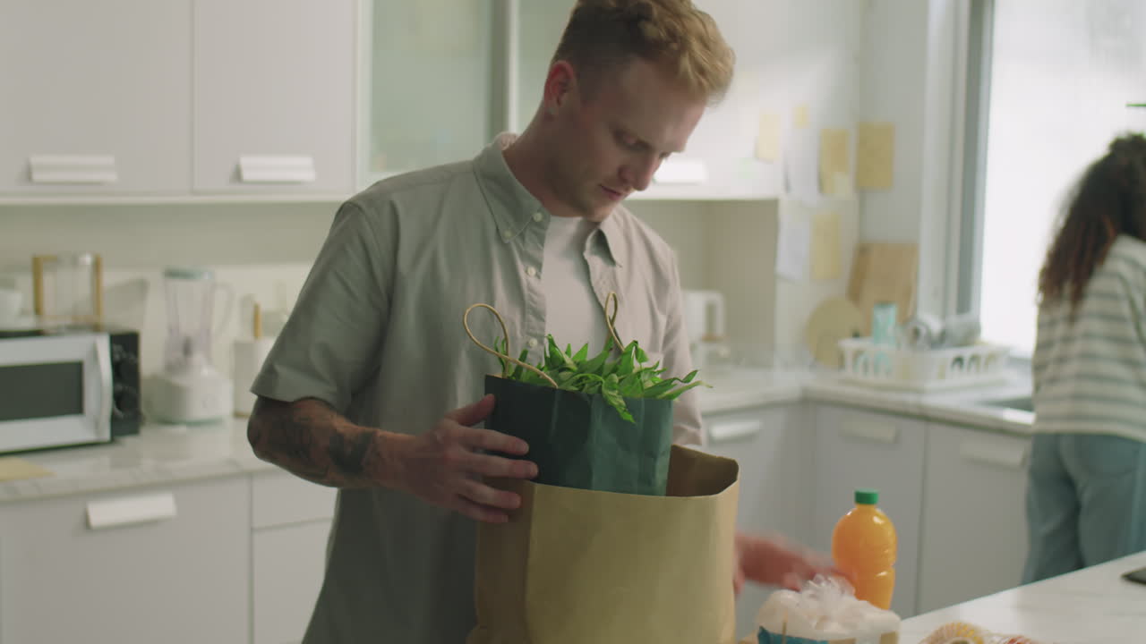 Man Bringing Groceries and Talking with Wife Doing Dishes
