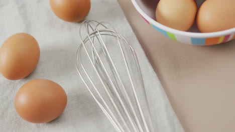 video of overhead view of eggs and egg whisk on rustic cloth on beige background