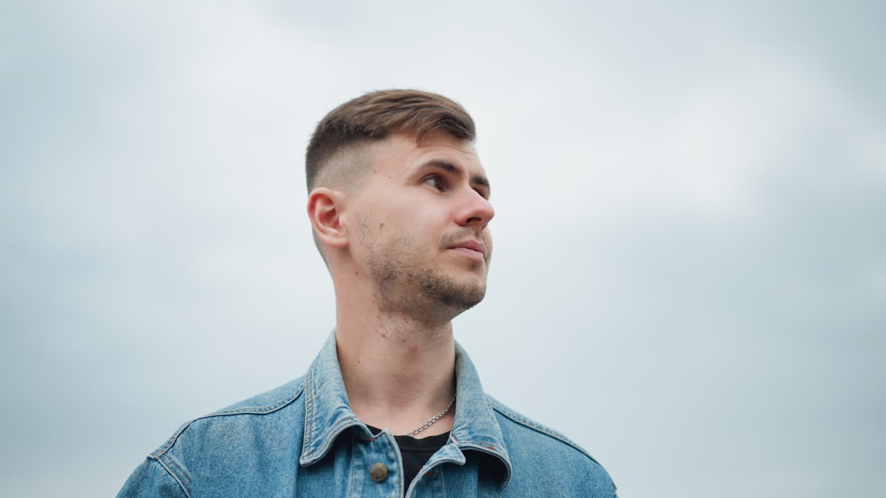 Uomo giovane che esce, giovane uomo caucasico con giacca di jeans in piedi all'aperto con cielo aperto, giovane uomo caucasico che indossa abiti di jeans che esce dal veicolo in mezzo alla natura e al cielo nuvoloso