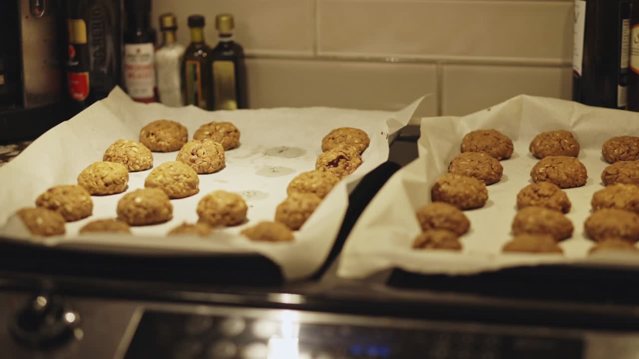 Person Takes Freshly Baked Oatmeal Cookies Cooling On Parchment-lined Baking Sheets On Tray. - handheld shot