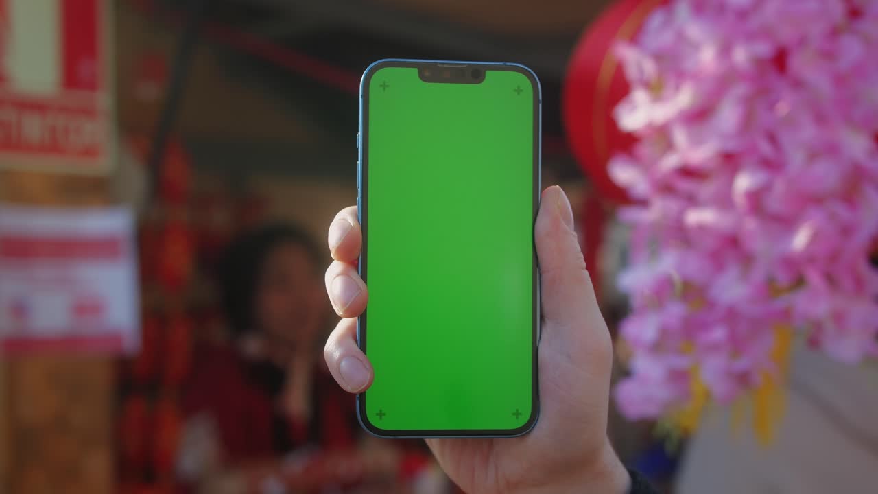 Young man holding phone chroma key screen on the street in front of chinese lignt close-up. Male with green screen on smart phone swiping .