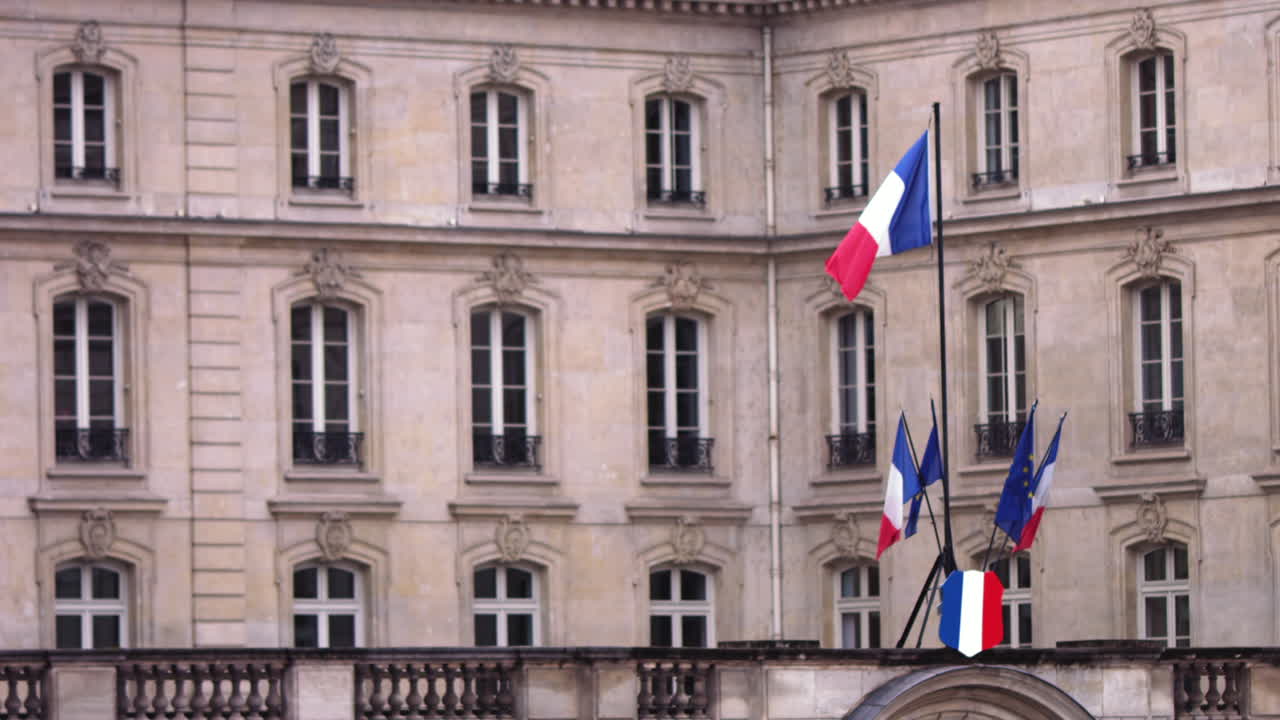 Slow motion footage of a small french flag that is moving in the wind in front of a government building in Paris, France