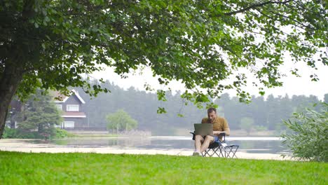 man working with laptop in field with lake view.