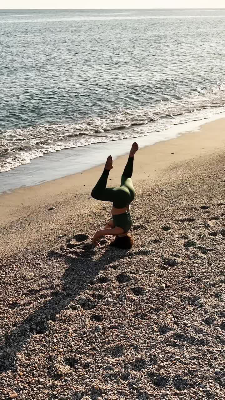 Active female in sportswear practicing headstand on beach