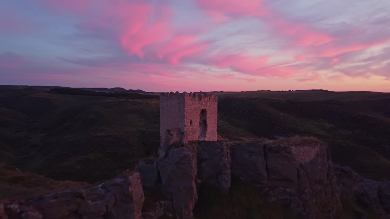 Drone shot of the medieval Oreja Castle perched on a hilltop at golden hour near Aranjuez, Spain. Scenic sunset over rural fields and rocky landscape.