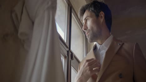 man looking out of window in a beige suit