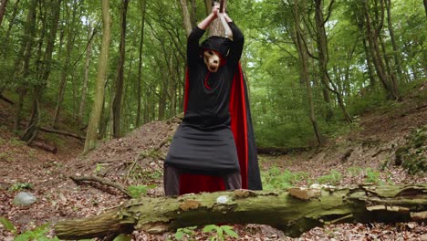 man in grim reaper and animal skull face costume poked scythe on the ground in the forest