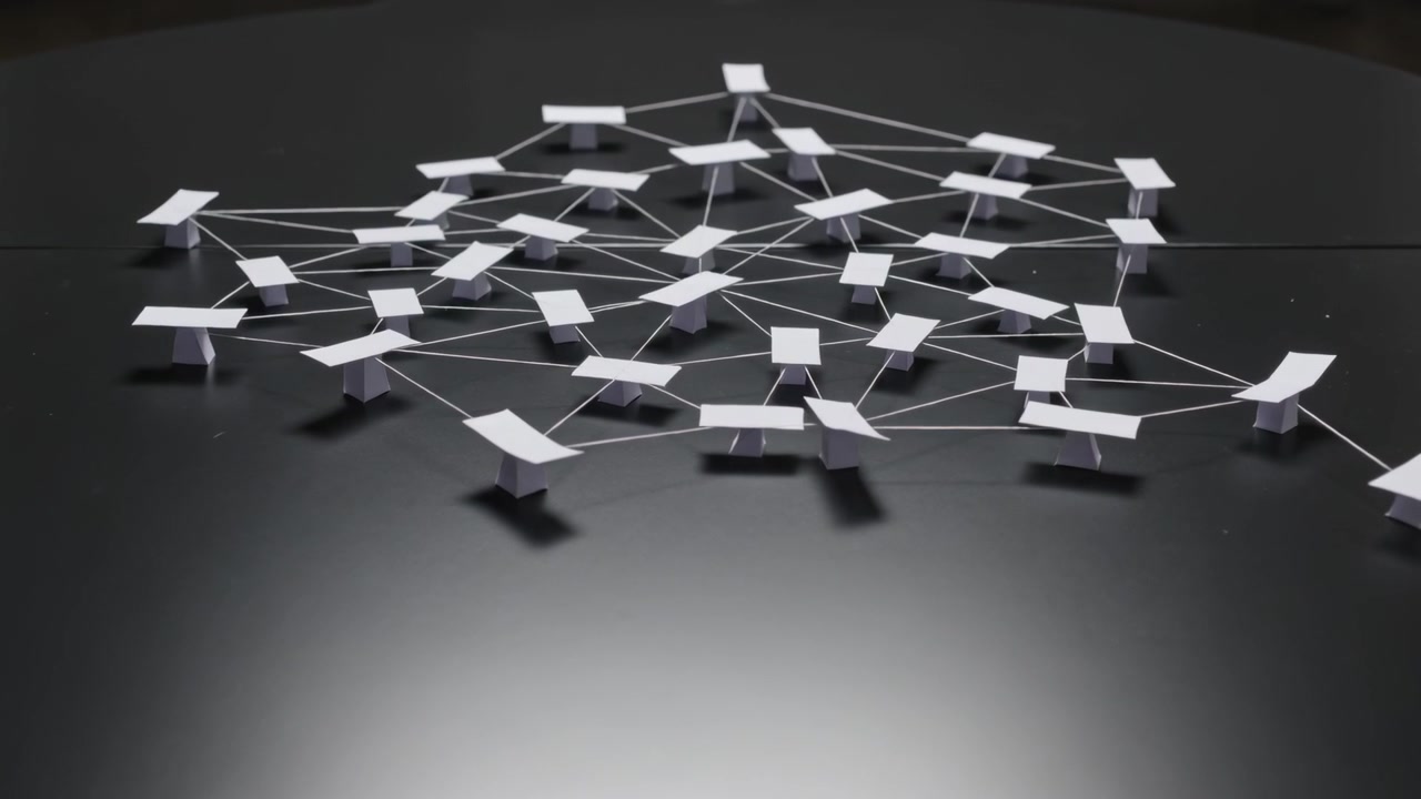 Lowering camera revealing white paper nodes, thin strings casting shadows on glossy black tabletop
