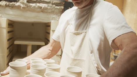 smiling senior caucasian man wearing apron taking fired pots from kiln at pottery workshop