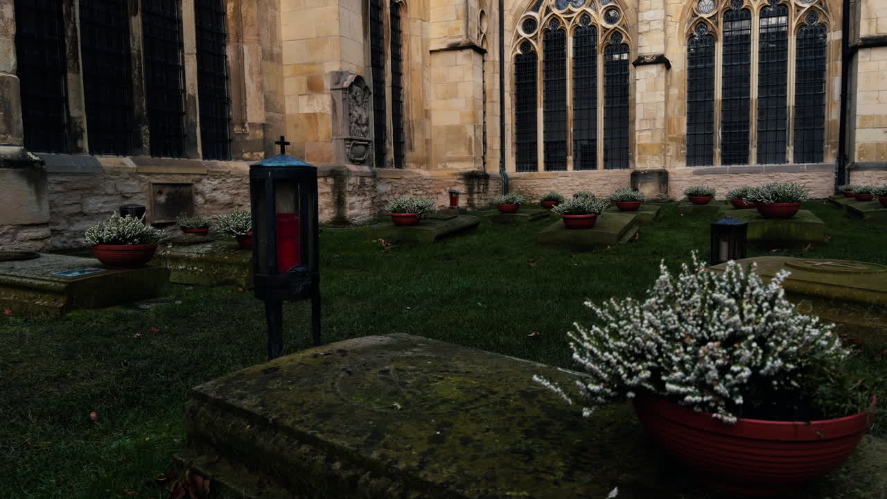 Cimitero storico del chiostro presso il Duomo di San Paolo a Münster, Germania. Tombe in pietra e lanterne commemorative nel cortile della cattedrale creano un'atmosfera tranquilla di ricordo e fede.