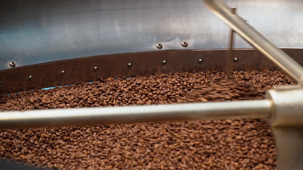 Close up of a large batch of roasted coffee beans being stirred inside a coffee roasting machine