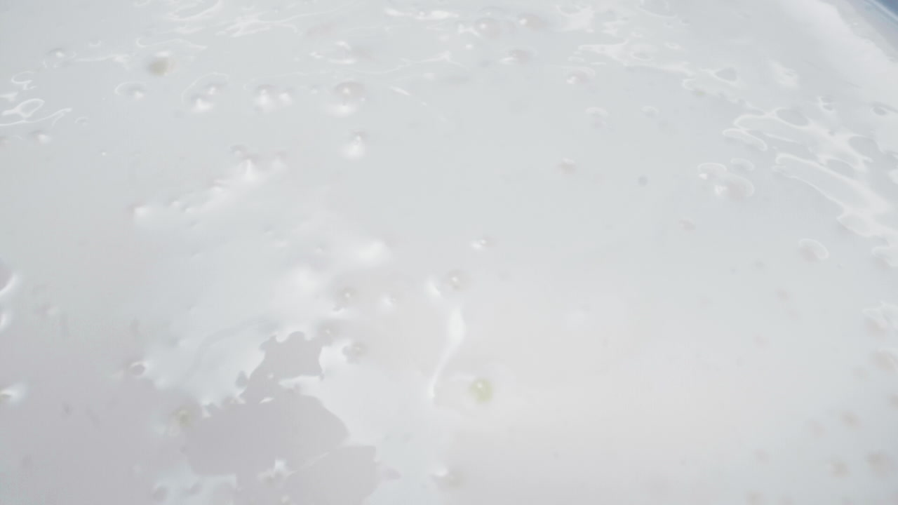 Slow motion close-up shot of fresh mango cubes falling into a bowl of smooth white yogurt. The vibrant yellow contrasts beautifully with the creamy white texture, creating a visually delicious moment.