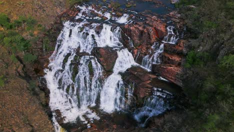 aerial view ofcataratas dos couros, a breathtaking waterfall cascading over red rock formations in the lush landscape of chapada dos veadeiros national park, goiás, brazil, drone dolly tilting down