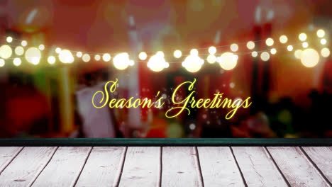 Seasons-greetings-text-and-glowing-yellow-fairy-light-decoration-hanging-over-wooden-plank