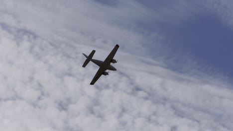 a twin prop light aircraft flies overhead silhouetted by the clouds