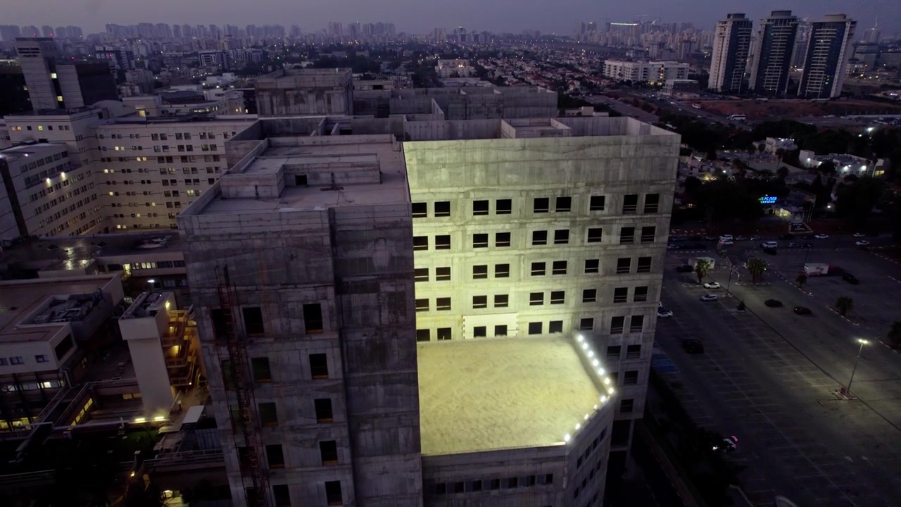 Vista aérea con dron de un edificio comercial de gran altura en construcción con andamios visibles y estructura de hormigón, situado en el horizonte de Petah Tikva.