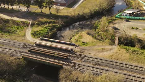 AERIAL---Woman-jogging-over-bridge,-river-and-railway-in-Maschwitz,-Argentina