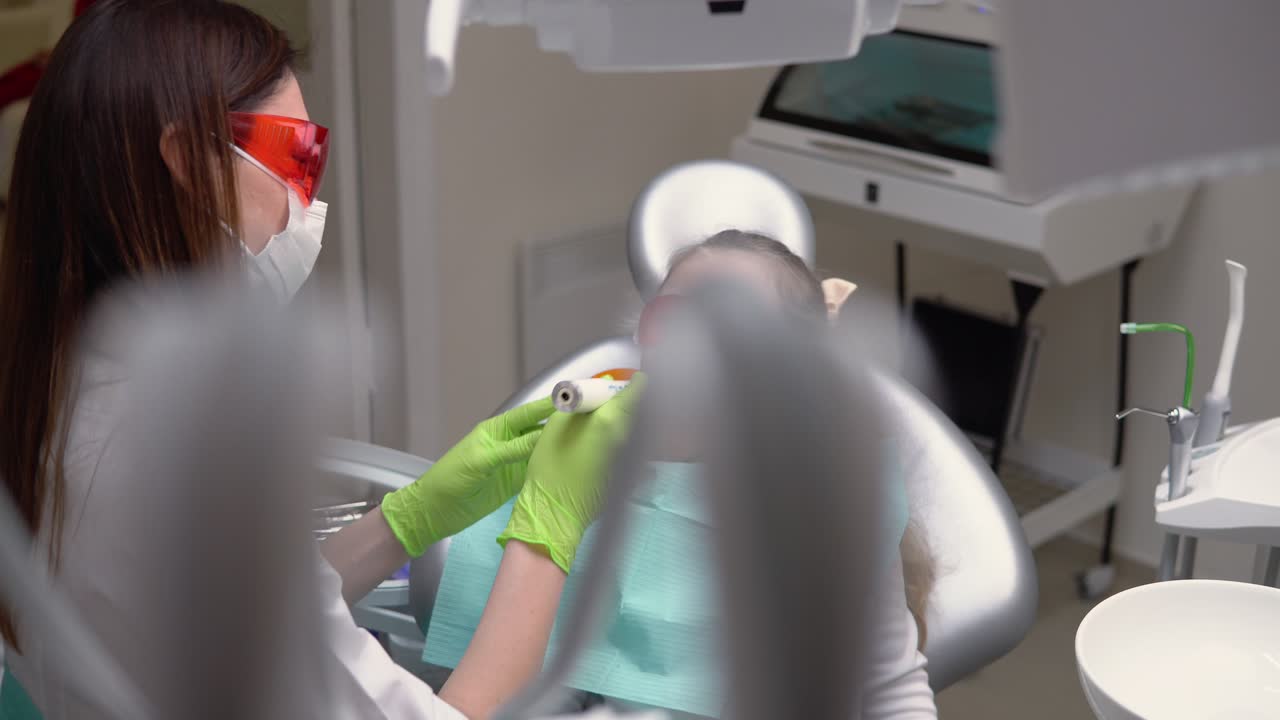 una niña linda en la clínica del dentista recibe tratamiento dental para llenar una cavidad en un diente. restauración dental y polimerización de material con luz uv. filmado en 4k