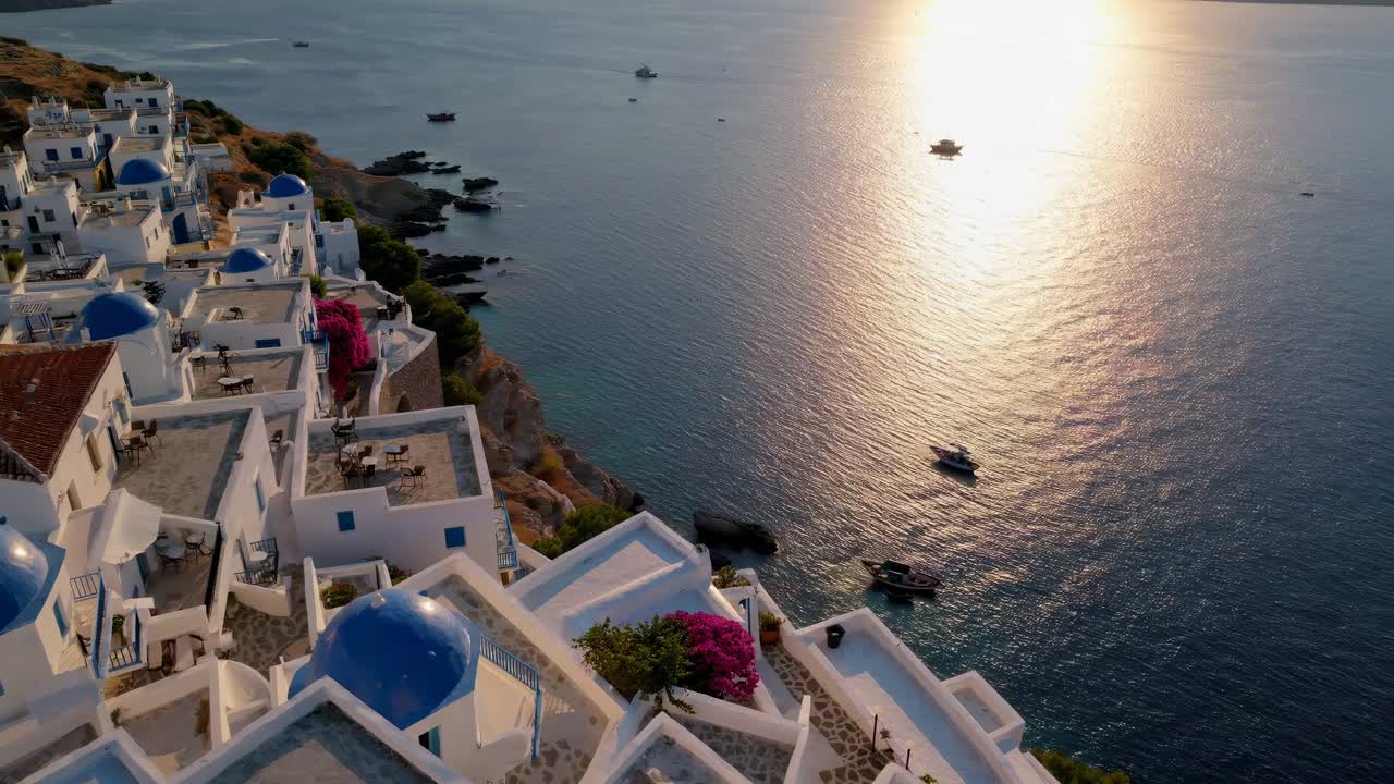 Aerial video captures a serene coastal village with white buildings and blue domes at sunset